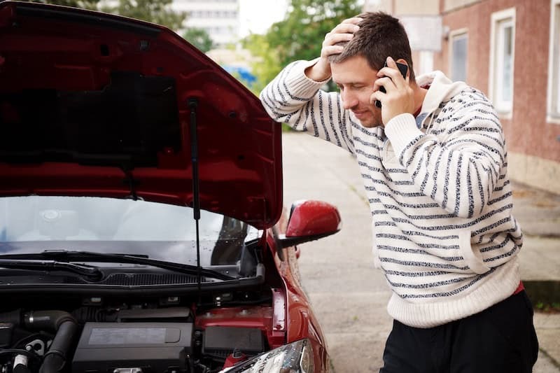 homme téléphonant devant le capot ouvert de sa voiture en panne